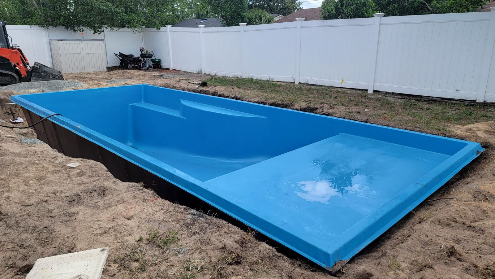 Rectangular fiberglass pool shell with tanning ledge set in an excavation