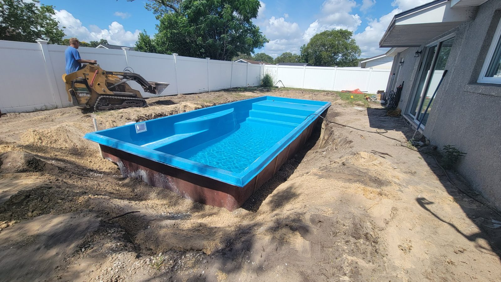 Crew backfilling around a fiberglass pool shell with a compact loader