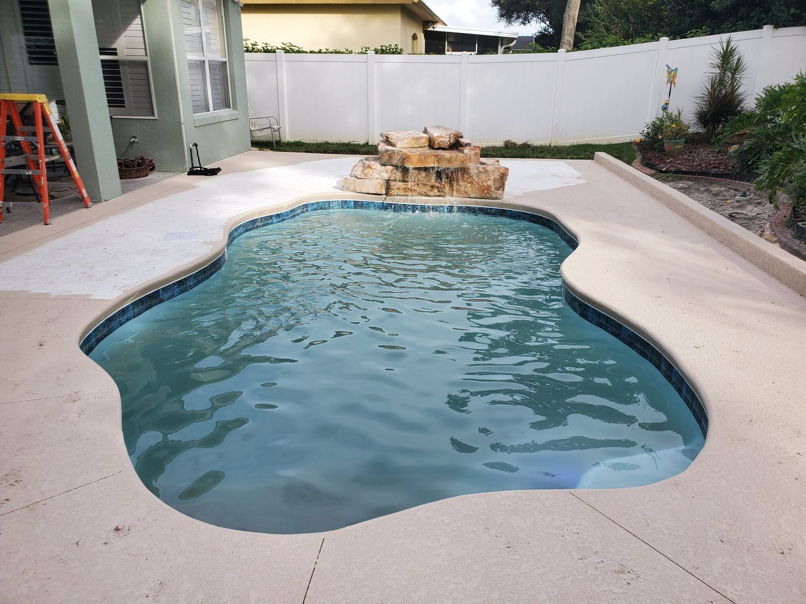 Concrete pool deck with a rock waterfall and acrylic coating in progress