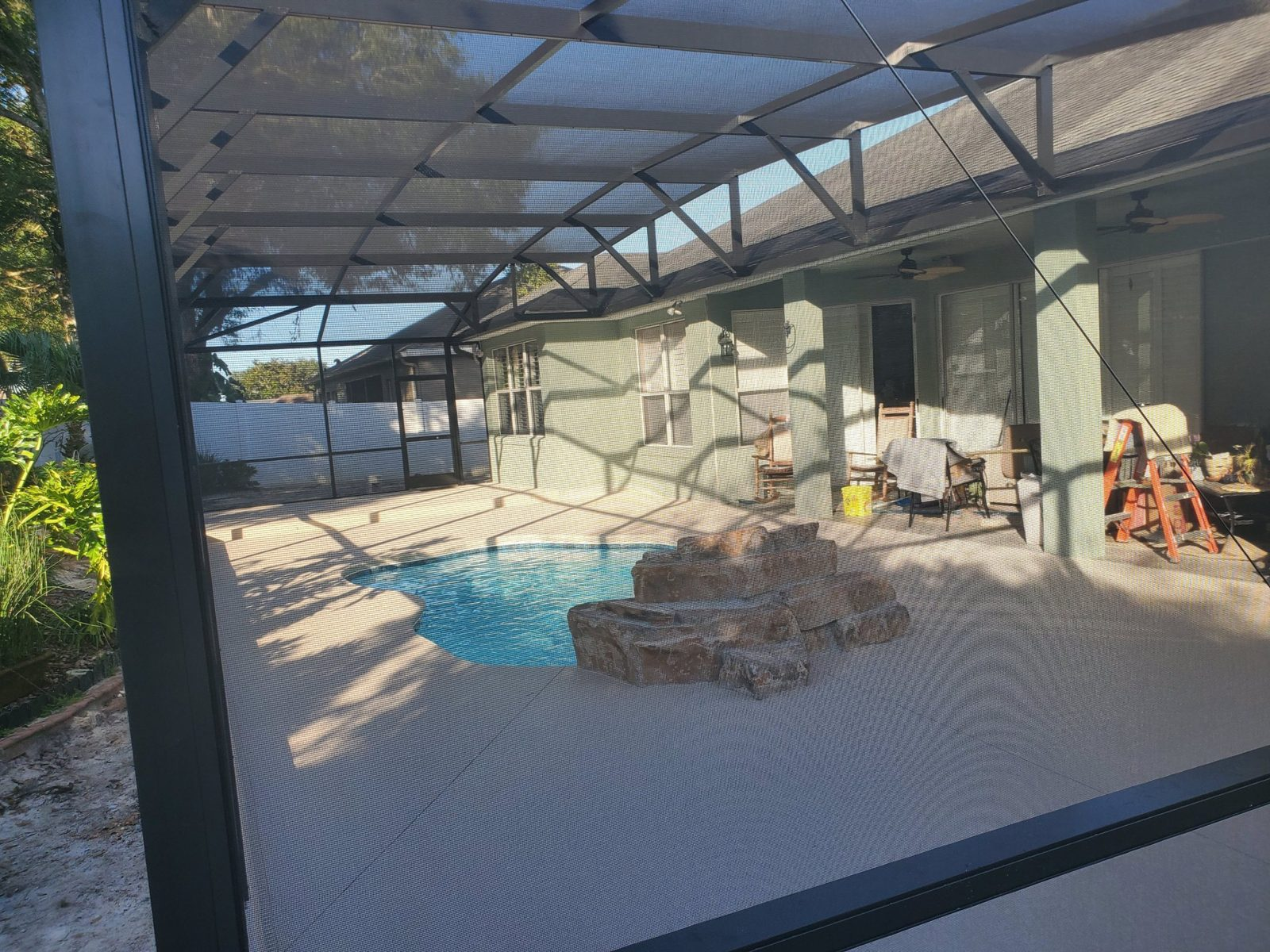 Screen enclosure framing over a fiberglass pool with a rock waterfall