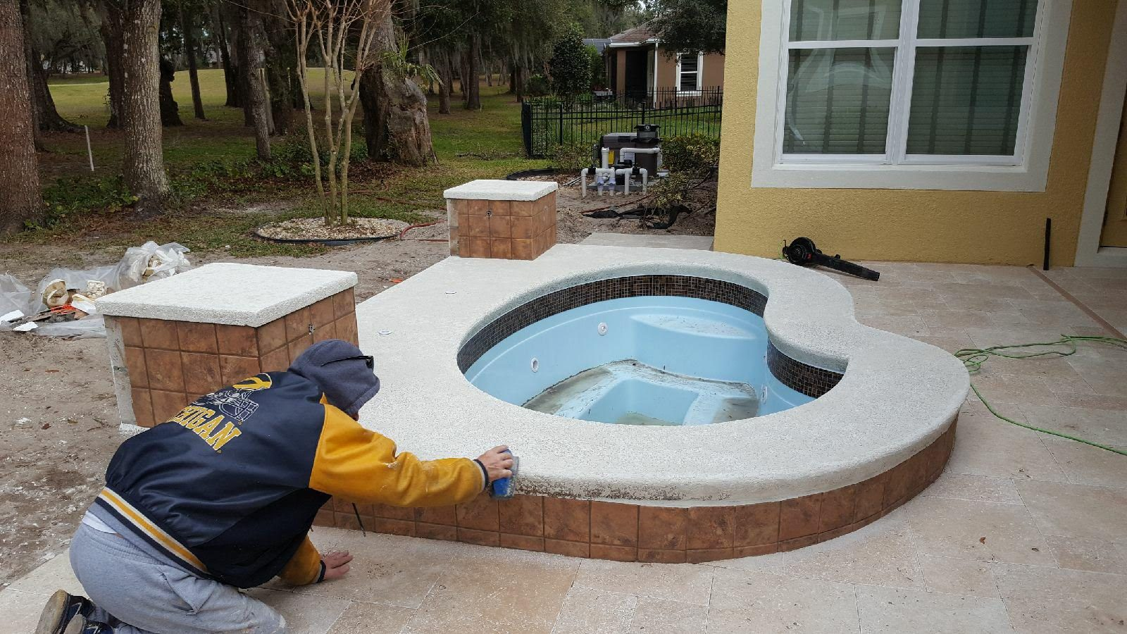 Worker texturing the coping cap of a raised tiled spa