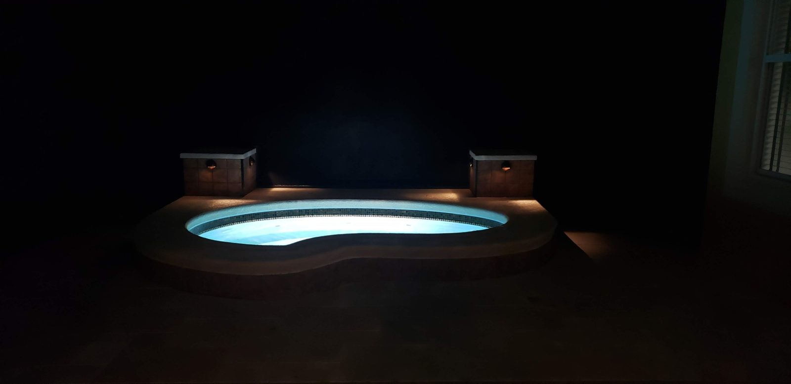 Raised spa lit at night with deck lights on the pillars