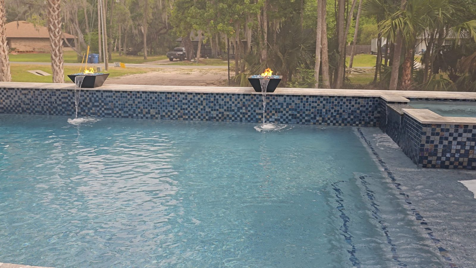 Fire and water bowls on a glass tile raised wall of a custom pool