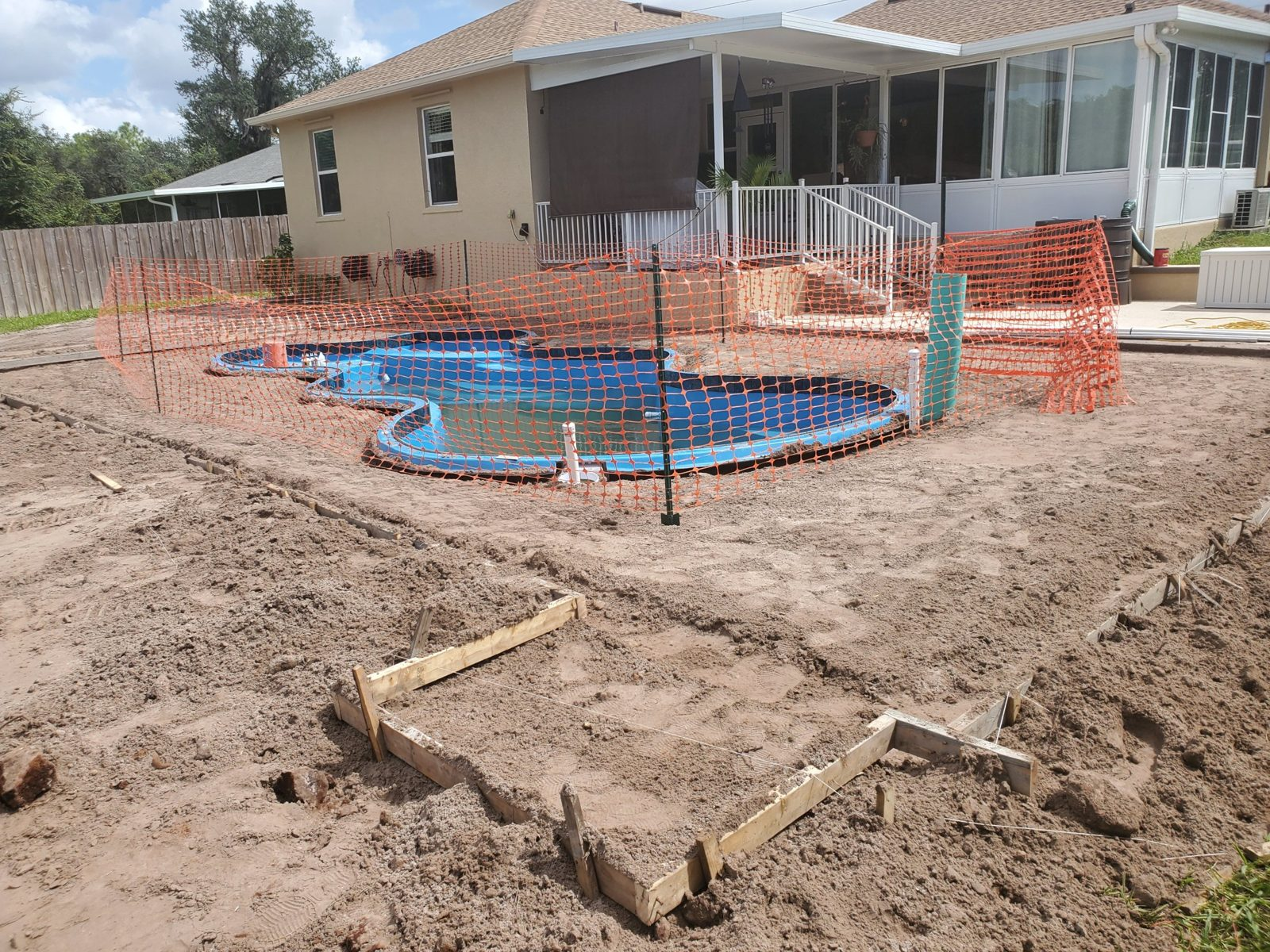 Fiberglass pool shell backfilled with concrete deck forms beside an elevated porch