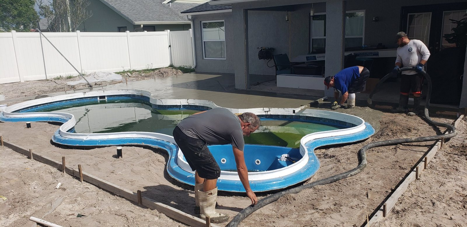 Crew pouring a concrete pool deck around a fiberglass pool
