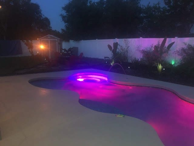 Fiberglass pool and attached spa lit with LED lights at dusk